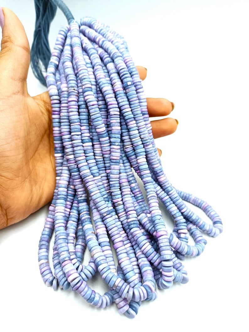 May include: A bundle of light blue and lavender disc-shaped beads. The beads are held together by a dark blue string. The beads are small and uniform in size, with a slightly iridescent finish. The beads are likely for jewelry making.