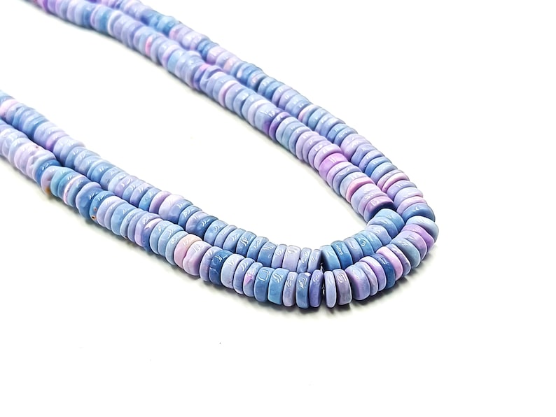 May include: A close-up of two strands of light blue and lavender gemstone beads. The beads are flat, round, and uniform in size. The background is plain white, highlighting the colors and textures of the beads. The beads are likely used for jewelry making.