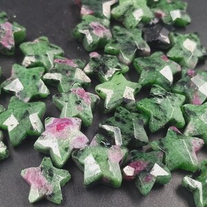 May include: A scattering of star-shaped gemstones in green and pink hues. The faceted stones have a polished finish, with a mix of opaque and translucent sections. These gemstones could be used for jewellery making or other crafts.