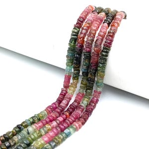 May include: Strands of colorful tourmaline beads in shades of pink, green, and brown. The beads are small, flat, and rectangular, strung together to create a multi-colored effect. The beads are displayed against a white background.