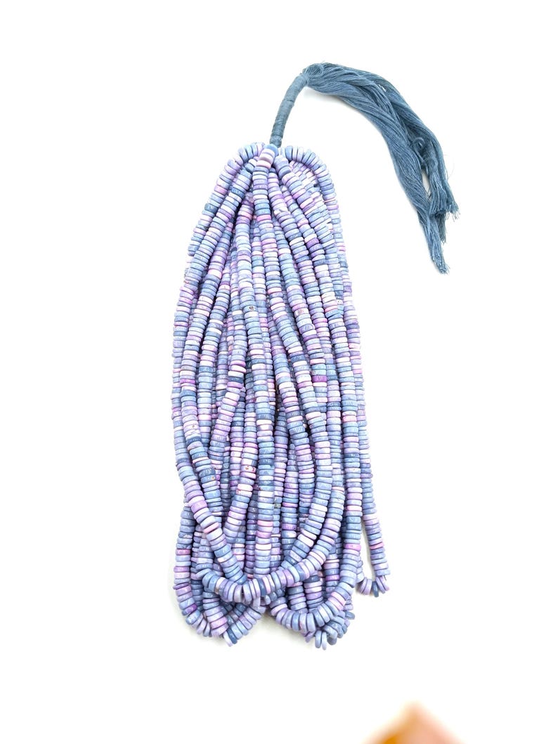 May include: A bundle of disc-shaped beads in shades of blue, purple, and white, tied together with a blue tassel. The beads are strung together, creating a cascading effect. The background is plain white.