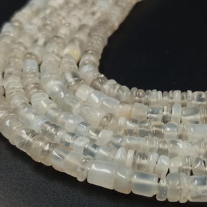 May include: Close-up of several strands of translucent, off-white gemstone beads. The beads are rectangular and have a slightly rounded shape. The beads are strung together, creating a necklace or bracelet.