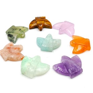 Peut inclure: Une collection de huit figurines papillon en pierres précieuses sculptées de différentes couleurs, dont vert, orange, violet et rose. Les papillons sont disposés en cercle sur fond blanc.