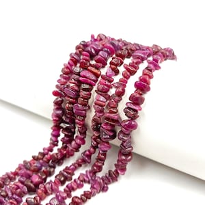 May include: A collection of multiple strands of small, irregular, tumbled ruby-colored gemstone chips. Each strand features a variety of deep magenta and dark pink stone fragments with a polished, glossy finish, arranged in a cascading vertical pattern.
