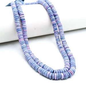 May include: Two strands of a necklace made of flat, round beads in shades of blue and lavender. The beads are uniform in size and shape, creating a layered effect. The necklace is displayed against a white background.