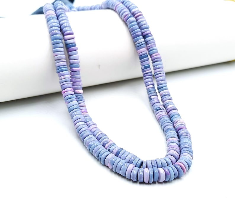 May include: Two strands of a necklace made of flat, round beads in shades of blue and lavender. The beads are uniform in size and shape, creating a layered effect. The necklace is displayed against a white background.