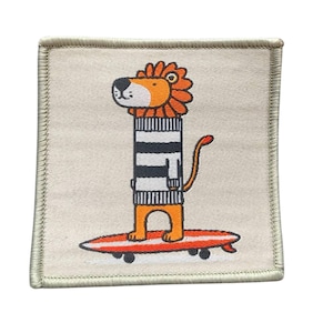 Könnte beinhalten: Ein beigefarbener Stoff-Patch mit einem Löwen, der einen gestreiften Pullover trägt und auf einem Surfbrett reitet. Der Löwe hat orangefarbenes Fell und eine Mähne, und das Surfbrett ist rot mit weißen Streifen.