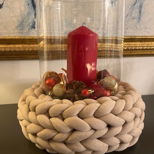 Könnte beinhalten: Ein beigefarbener geflochtener Seilring mit einem Glaszylinder, gefüllt mit einer roten Kerze, goldenen und roten Ornamenten und Tannenzapfen.