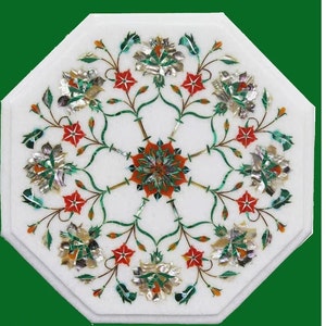 May include: White marble octagonal table with inlaid floral design. The design features red, green, and silver-coloured flowers and leaves arranged in a symmetrical pattern. The table is a decorative piece.