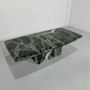 Op de afbeelding: Een rechthoekige salontafel van groen marmer met donkere adering. De tafel heeft een massieve, blokachtige basis en een glad, gepolijst oppervlak. Het marmer heeft een natuurlijk, organisch patroon.