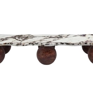 Può includere: Un tavolino decorativo con un piano in marmo bianco con venature scure. Il tavolo è sostenuto da quattro gambe sferiche, marrone-rossastro. Il piano del tavolo ha una forma organica unica.