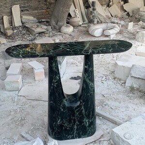 Puede incluir: Una mesa consola de mármol verde con un diseño único y abstracto. La mesa tiene una tapa larga y ovalada y una base esculpida única.