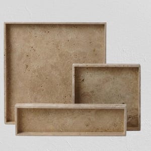 May include: A collection of four rectangular trays in different sizes. The trays are crafted from a light brown stone with a textured finish. The trays are arranged in a nested configuration, with the largest at the rear and the smallest at the front.
