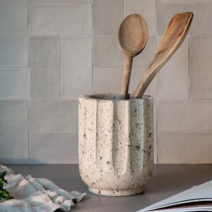 Peut inclure: Un pot à ustensiles de cuisine beige et texturé avec des rainures verticales, contenant une cuillère et une spatule en bois. Le pot est fait d'un matériau semblable à de la pierre. Le fond présente un mur carrelé.
