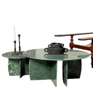 May include: A green marble coffee table with a round top and four legs. The table is made of two pieces, one larger and one smaller. The smaller piece is placed on top of the larger piece. There are two black candle holders and a white candle on the smaller piece.