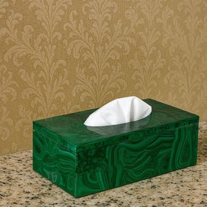 May include: A rectangular tissue box with a malachite green finish. The box has a swirling pattern and a white tissue peeking out of the top. The box is sitting on a speckled surface.