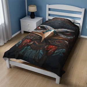 May include: A twin-sized bedspread featuring a detailed illustration of an eagle's face. The design incorporates shades of black, brown, red, and teal, with intricate feather and pattern details. The bedspread is placed on a white bed frame in a room with blue walls.