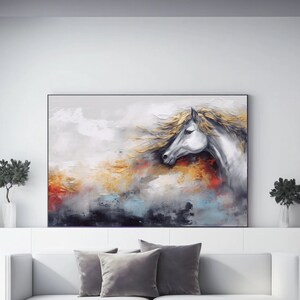 May include: A painting depicting a white horse with a flowing mane against a colourful abstract background. The painting is framed and hangs on a white wall above a white sofa with grey throw pillows.