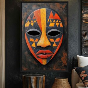May include: A framed African mask with a black background. The mask features a symmetrical design with orange, yellow, and black geometric patterns. The mask has black eye holes and red lips. The artwork is displayed above a wooden side table and a textured vase.