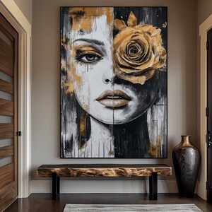 May include: Abstract painting of a woman's face with a large golden rose covering one eye. The painting is in a black frame and is hanging on a wall above a wooden bench.