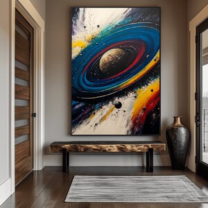 May include: A colorful abstract painting of a galaxy with a large planet in the center surrounded by rings. The painting is framed in black and hanging on a wall in a hallway.