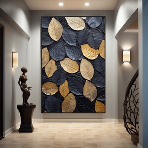 Peut inclure: Une grande œuvre d'art murale rectangulaire représentant un motif en relief de feuilles superposées. Les feuilles sont dans des tons or et bleu foncé, sur un fond noir texturé. L'œuvre est encadrée en noir et est accrochée dans un couloir.