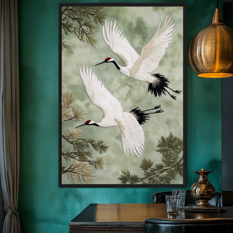 Puede incluir: Obra de arte enmarcada con dos grullas blancas en vuelo sobre un fondo verde y gris suave. Las grullas tienen marcas rojas en la cabeza y plumas negras en la cola. Se ven ramas de pinos.