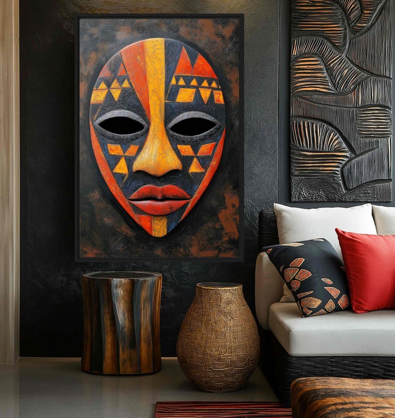May include: A framed African mask with a black background. The mask features a symmetrical design with orange, yellow, and black geometric patterns. The mask has black eye holes and red lips. The artwork is displayed above a wooden side table and a textured vase.
