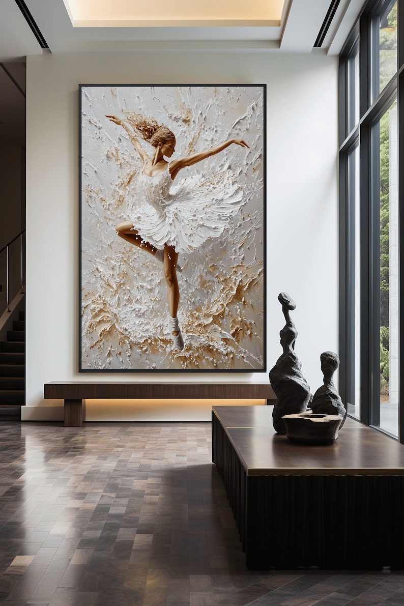 May include: A framed painting of a ballerina in a white tutu, dancing against a textured background of white and gold paint. The painting is hanging on a white wall in a modern interior.