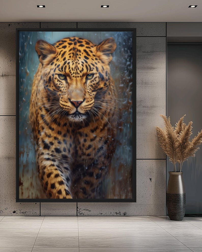 May include: A framed artwork featuring a detailed portrait of a leopard. The leopard has a tan coat with black spots and green eyes. The background has a blue and brown watercolor effect. The artwork is displayed on a gray wall.