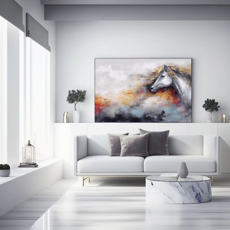 May include: A painting depicting a white horse with a flowing mane against a colourful abstract background. The painting is framed and hangs on a white wall above a white sofa with grey throw pillows.