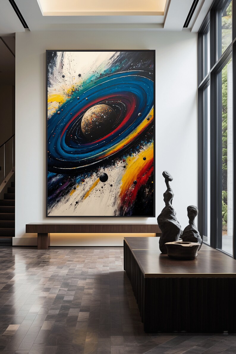May include: Abstract painting of a colorful galaxy with a planet in the center. The painting is framed in black and hanging on a white wall in a modern interior.