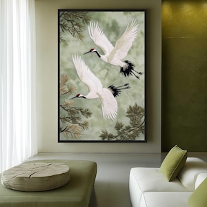 Puede incluir: Una obra de arte enmarcada que presenta dos grullas blancas en vuelo sobre un fondo verde y gris suave. Las grullas tienen marcas negras y rojas, con plumas de ala detalladas. La obra de arte est&aacute; enmarcada en un borde negro, con ramas de &aacute;rboles en las esquinas.