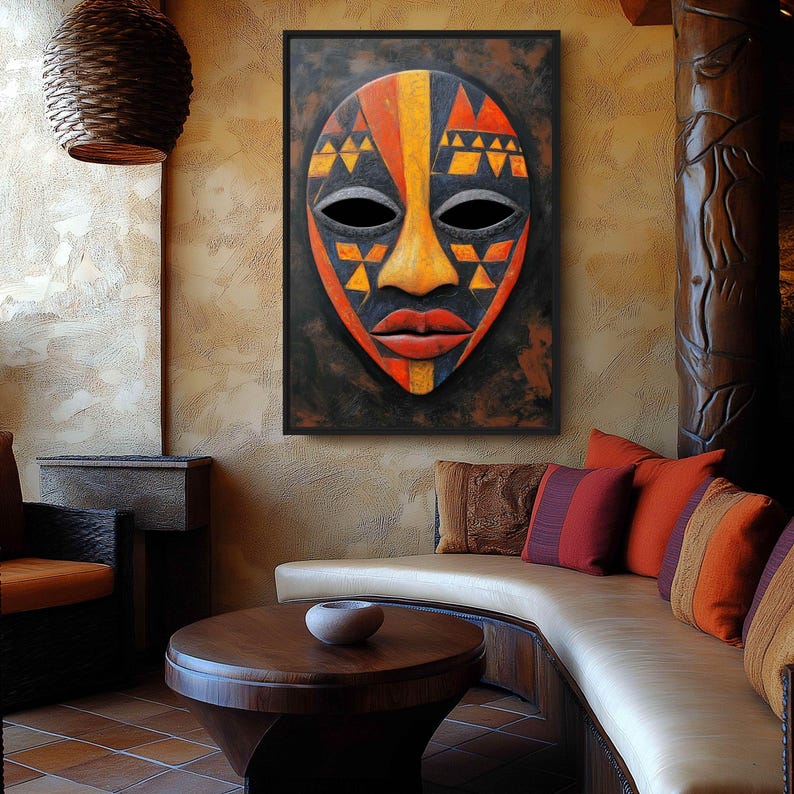 May include: A framed, colorful African mask with a black background. The mask features geometric patterns in orange, yellow, and black, with a prominent orange nose and red lips. The mask is displayed on a textured wall in a room with a curved sofa and decorative pillows.