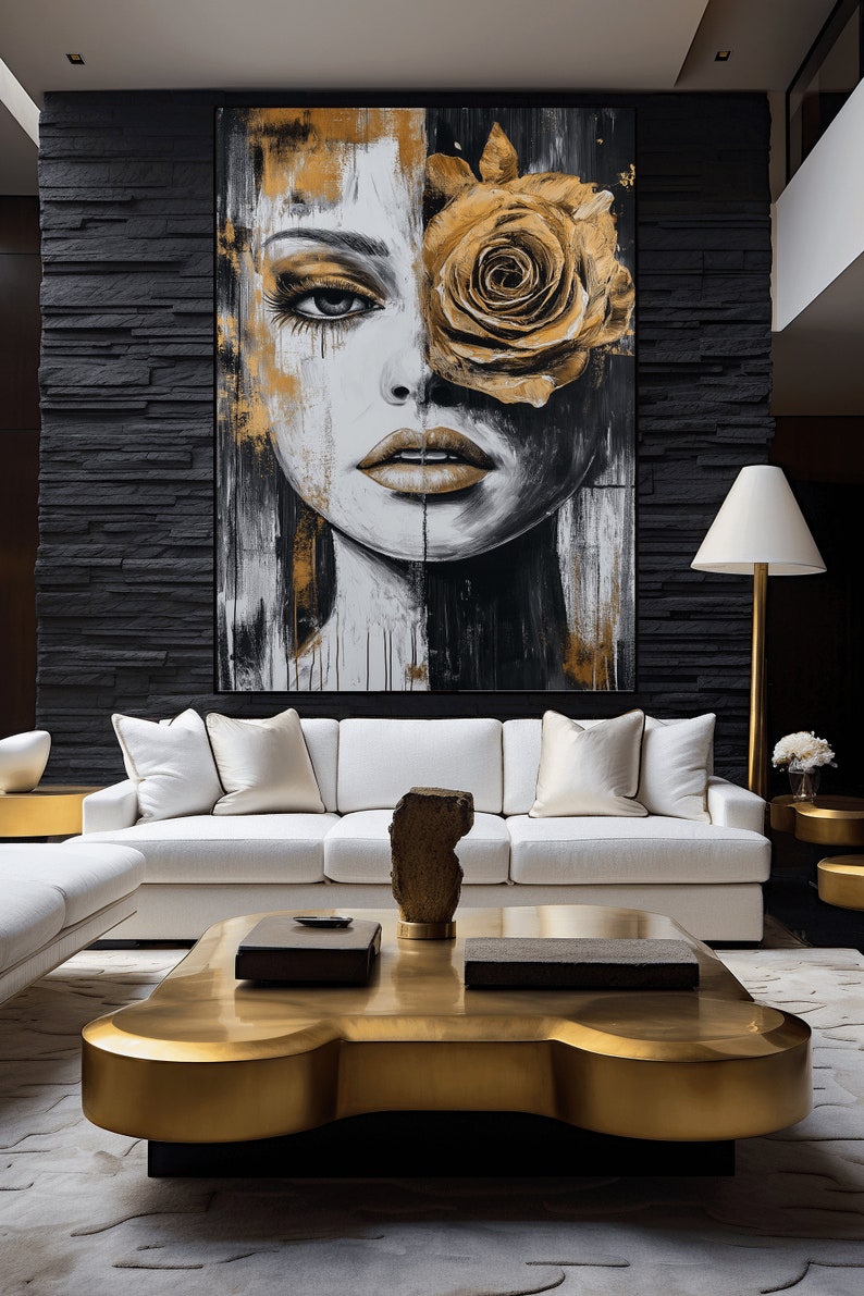 May include: A white sofa with gold throw pillows sits in front of a black wall with a large abstract painting of a woman's face with a gold rose covering one eye. A gold coffee table with a unique shape sits in front of the sofa.