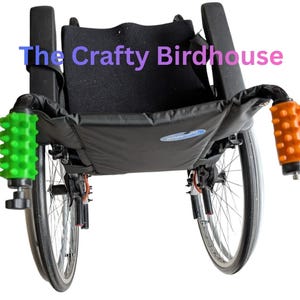 May include: A black wheelchair with a black seat and backrest. The armrests have green and orange textured grips. The text "The Crafty Birdhouse" is across the top of the image.
