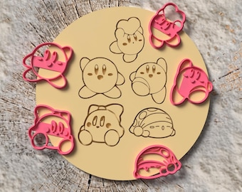 May include: A collection of pink and beige cookie cutters featuring various designs of a cartoon character. The cutters are arranged on a circular beige surface with etched character outlines. The background is a wooden surface.