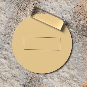 Peut inclure: Un cercle beige avec un contour rectangulaire noir et un objet rectangulaire transparent au-dessus. Les objets sont sur une tranche de bois avec une surface texturée de couleur claire.