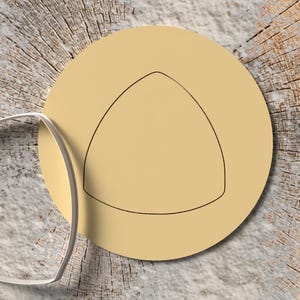 May include: A silver metal cookie cutter in the shape of a triangle is next to a tan circle with a triangle outline. The objects are on a wood surface.