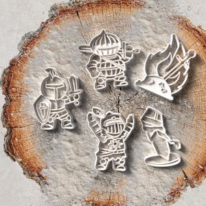 Peut inclure: Cinq emporte-pièces argentés sur le thème des chevaliers. Les emporte-pièces sont disposés sur une tranche de bois, avec un fond en marbre. Les motifs de chevaliers comprennent un chevalier avec une épée et un bouclier, un chevalier avec une arme et un chevalier avec les bras levés.