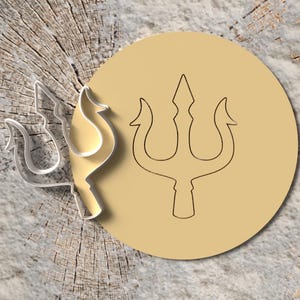 Könnte beinhalten: Ein Dreizack-Design, ein dreizackiger Speer, ist auf einem hellbraunen kreisförmigen Hintergrund abgebildet. Eine transparente Kunststoff-Dreizack-Form befindet sich neben dem beigen Kreis. Der Hintergrund ist eine hellbraune Holzmaserung.