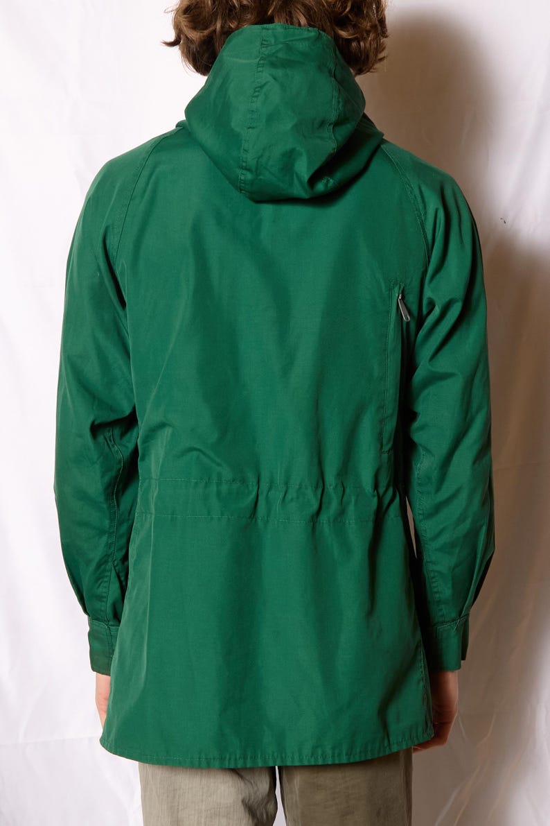 Op de afbeelding: Een groene capuchonjas met een ritssluiting en een trekkoord in de taille.