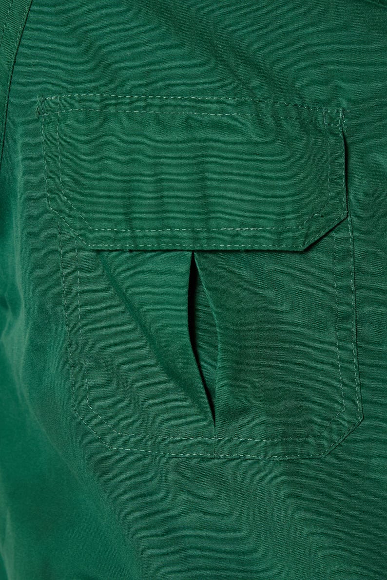 Op de afbeelding: Een donkergroen utility shirt met een grote, gestikte zak aan de voorkant. De zak heeft een klep met een kleine opening aan de bovenkant.