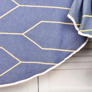 Könnte beinhalten: Ein blaues Textil mit einem geometrischen Muster aus gelben Linien. Der Stoff hat einen weißen Rand. Ein Teil des Textils ist gefaltet und zeigt gelbe Streifen und einen weißen Rand. Der Hintergrund ist eine weiße, geriffelte Oberfläche.
