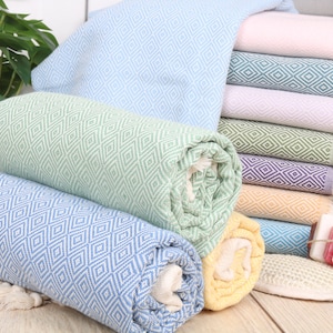 May include: A collection of colorful, rolled and stacked diamond-patterned towels. The towels are in shades of blue, green, yellow, pink, and purple. Some towels are rolled, while others are neatly stacked. The towels have fringed edges.