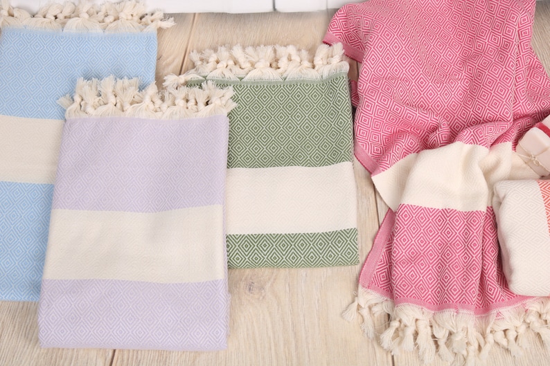 May include: A collection of colorful Turkish towels with diamond patterns and fringed edges. The towels are in shades of blue, lavender, green, and pink, with white stripes. These lightweight towels are ideal for the beach or bath.