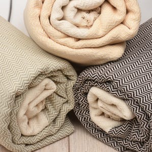 Könnte beinhalten: Drei gerollte Textilien mit Zickzackmuster. Eines ist beige, eines hellgrün und das dritte schwarz-weiß. Die Textilien sind eng gerollt und zeigen ein helleres Inneres. Der Hintergrund ist eine helle Holzoberfläche.