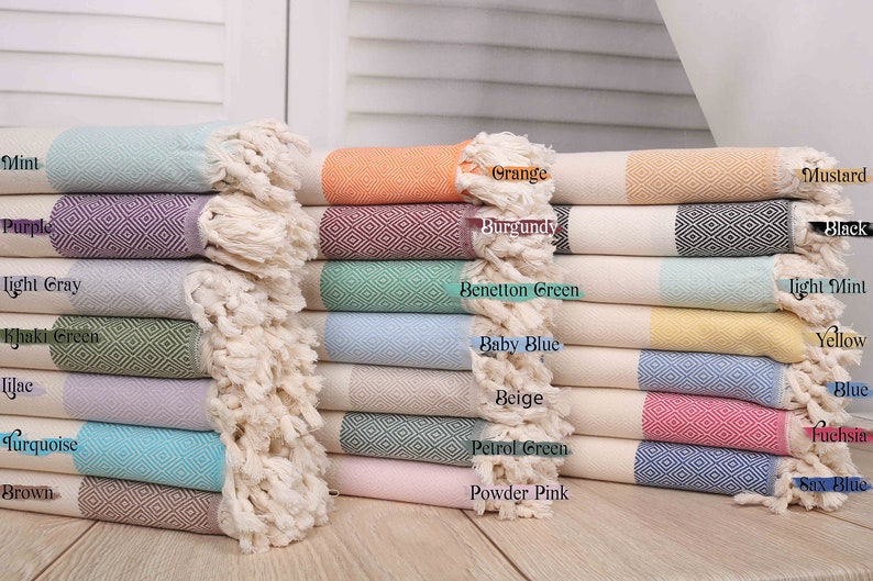 May include: A stack of colorful Turkish towels with diamond patterns and fringed edges. Colors include mint, purple, orange, burgundy, and mustard. The towels are made of soft, absorbent material, perfect for the beach or bath.