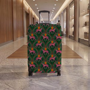 May include: A rolling suitcase featuring a repeating pattern of pink cheetahs on a dark green background. The design includes orange circular accents and white dotted semi-circular arches. The luggage has a black retractable handle and four wheels.