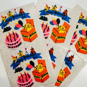 May include: A sheet of colorful birthday stickers featuring a teddy bear, balloons, candles, and a cake. The stickers have a fuzzy texture and say "Happy Birthday" on them.